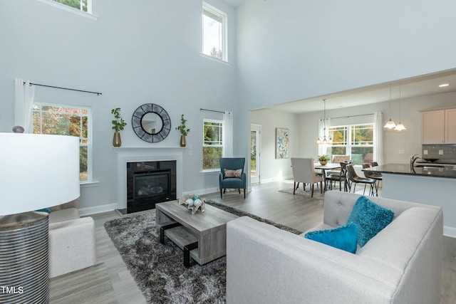 living room featuring sink, light hardwood / wood-style floors, a chandelier, and a high ceiling