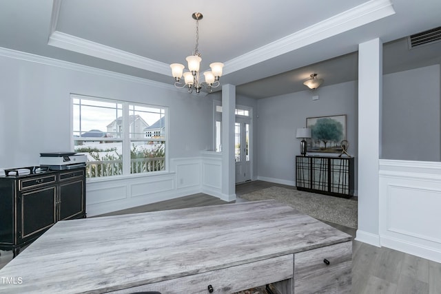 unfurnished dining area featuring a tray ceiling, wood-type flooring, ornamental molding, and a chandelier