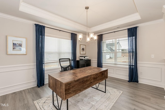 office space with a chandelier, light wood-type flooring, and a tray ceiling