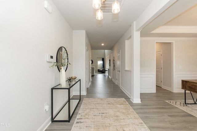 corridor with wood-type flooring, ornamental molding, and a chandelier