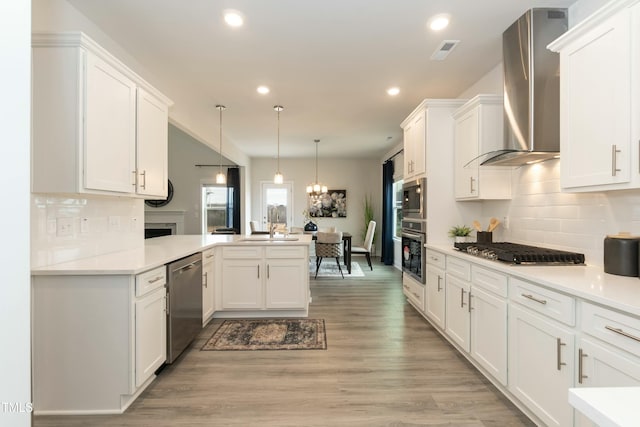 kitchen featuring appliances with stainless steel finishes, kitchen peninsula, pendant lighting, wall chimney range hood, and white cabinets