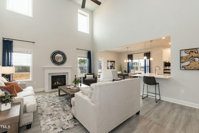 living room featuring sink, hardwood / wood-style flooring, ceiling fan, a towering ceiling, and a high end fireplace