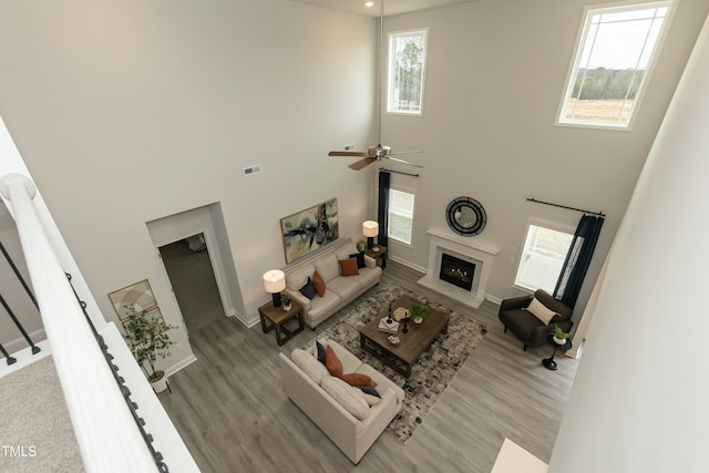 living room featuring a high ceiling, ceiling fan, light wood-type flooring, and a fireplace