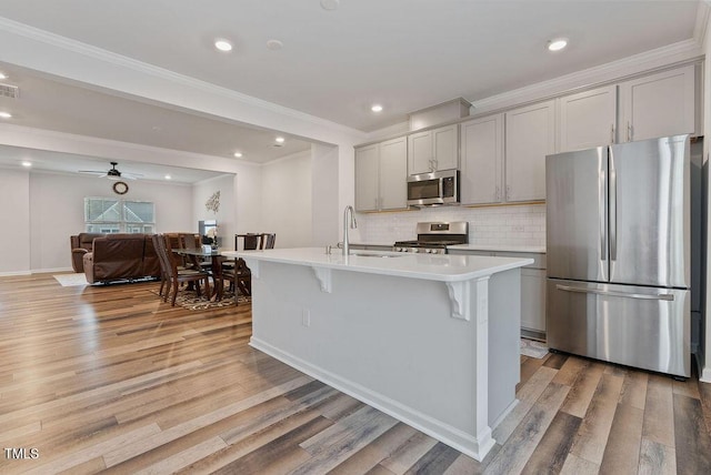 kitchen featuring light countertops, appliances with stainless steel finishes, a center island with sink, gray cabinetry, and a sink