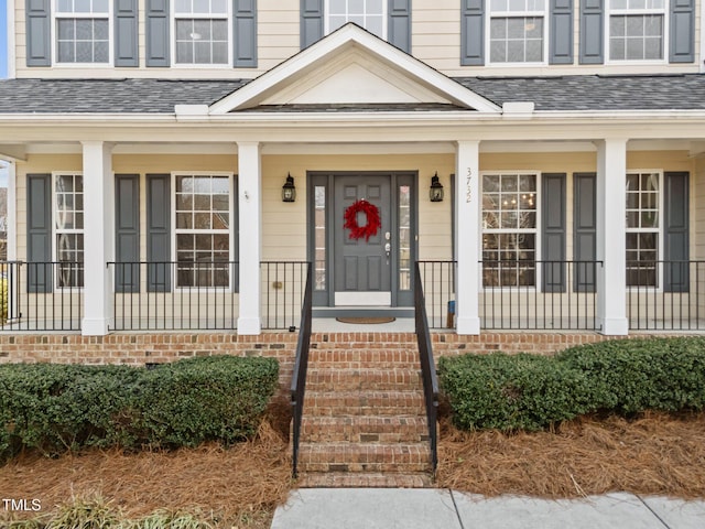 doorway to property with a shingled roof and a porch