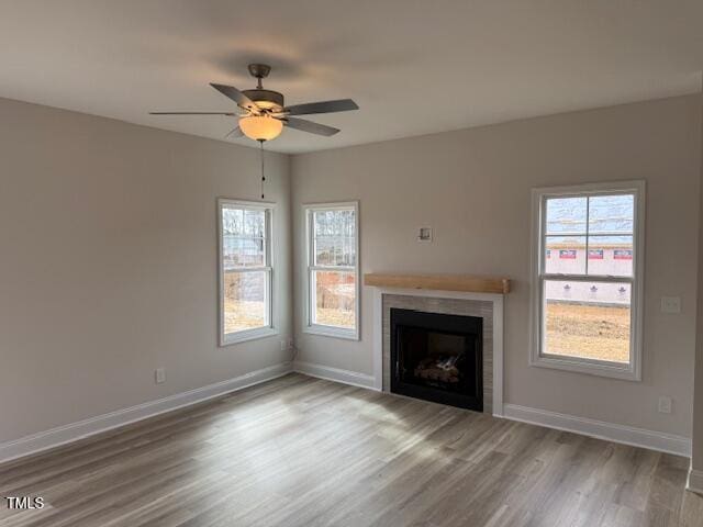 unfurnished living room with ceiling fan, a tile fireplace, wood finished floors, and baseboards