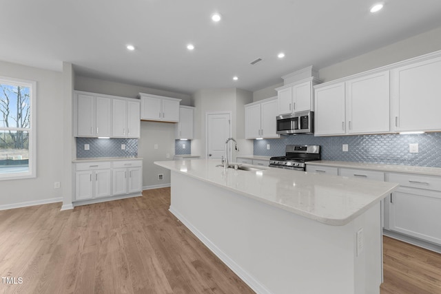 kitchen with appliances with stainless steel finishes, white cabinetry, sink, a kitchen island with sink, and light hardwood / wood-style floors