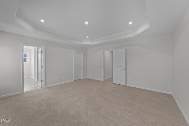 unfurnished bedroom with a raised ceiling, ornamental molding, light carpet, and ensuite bath