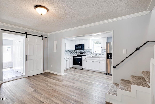 kitchen featuring sink, light wood-type flooring, stainless steel appliances, a barn door, and white cabinets