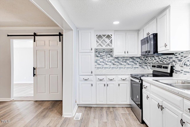 kitchen with white cabinetry, a barn door, light hardwood / wood-style floors, and stainless steel range with electric cooktop