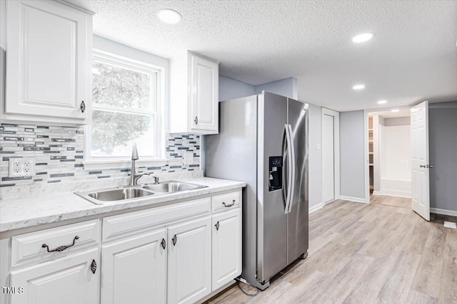 kitchen with sink, light hardwood / wood-style flooring, backsplash, white cabinets, and stainless steel fridge with ice dispenser