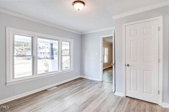 empty room with ornamental molding, a textured ceiling, and light wood-type flooring