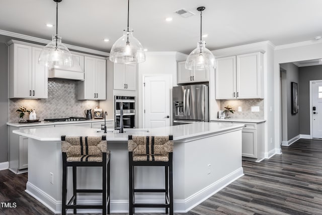 kitchen featuring stainless steel appliances, a kitchen bar, hanging light fixtures, and a center island with sink