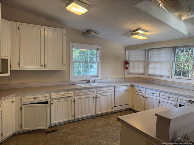 kitchen featuring vaulted ceiling, white cabinetry, sink, white dishwasher, and a textured ceiling