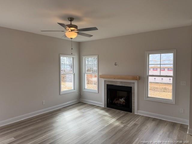 unfurnished living room with a fireplace, wood finished floors, a ceiling fan, and baseboards