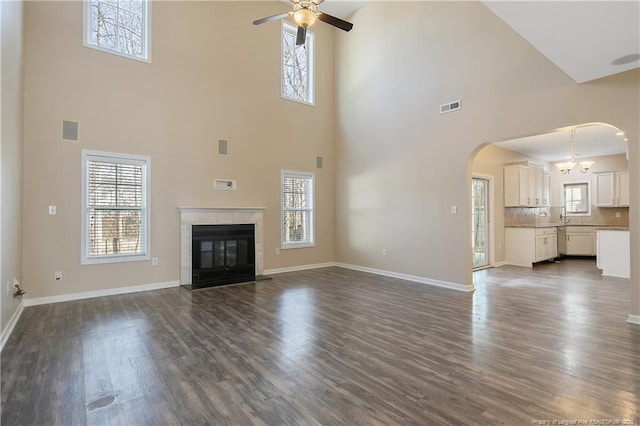 unfurnished living room featuring dark hardwood / wood-style flooring, sink, ceiling fan with notable chandelier, and a tile fireplace