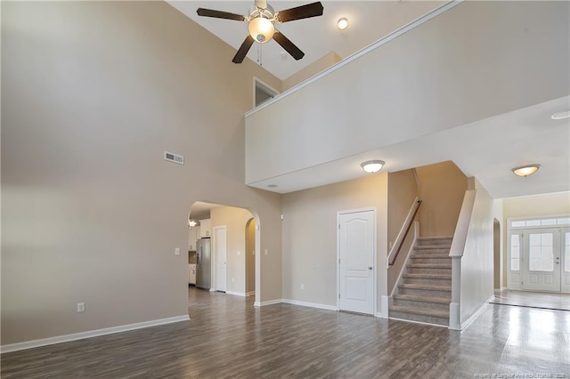 unfurnished living room with dark wood-type flooring, ceiling fan, and a high ceiling