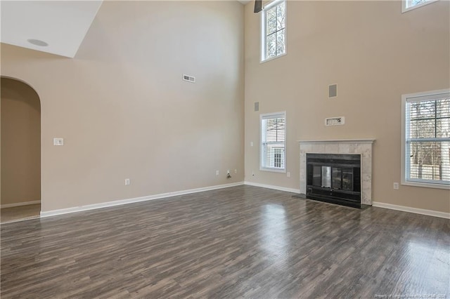 unfurnished living room featuring a towering ceiling, dark hardwood / wood-style flooring, and a tiled fireplace