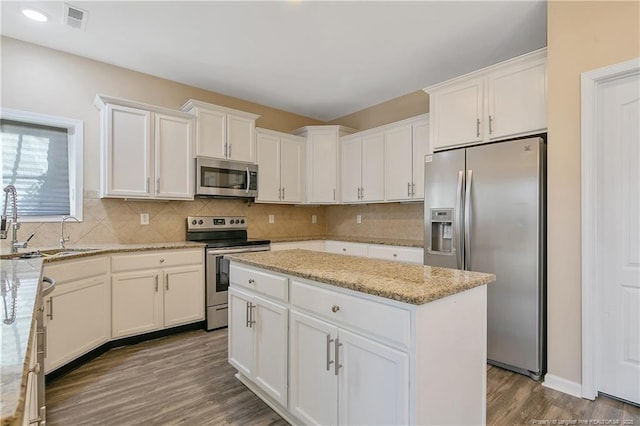 kitchen with appliances with stainless steel finishes, tasteful backsplash, white cabinetry, a center island, and light stone counters