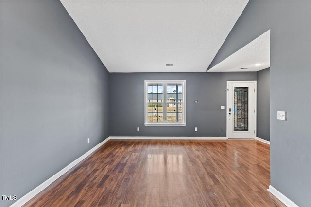 unfurnished room with hardwood / wood-style flooring, vaulted ceiling, and a textured ceiling