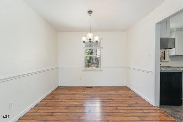 unfurnished dining area featuring hardwood / wood-style flooring and an inviting chandelier