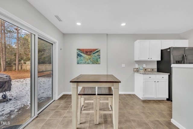 kitchen featuring white cabinetry, stainless steel fridge, light tile patterned flooring, and light stone counters