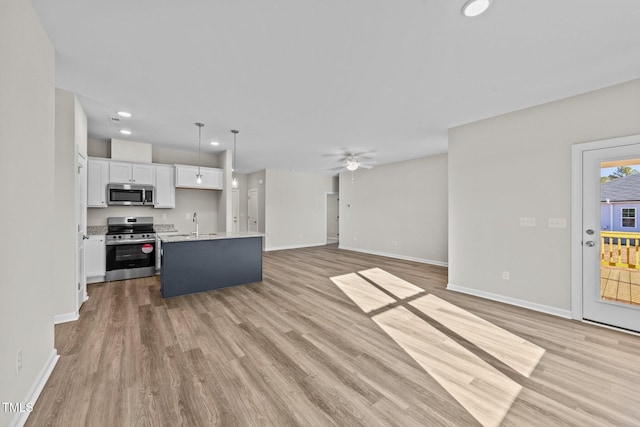 kitchen with appliances with stainless steel finishes, hanging light fixtures, light hardwood / wood-style floors, white cabinets, and a center island with sink