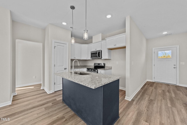 kitchen with appliances with stainless steel finishes, pendant lighting, sink, white cabinets, and a center island with sink