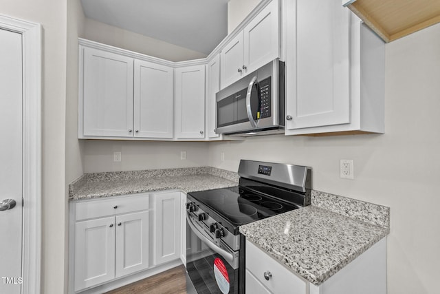 kitchen with appliances with stainless steel finishes, white cabinets, light stone counters, and light hardwood / wood-style flooring