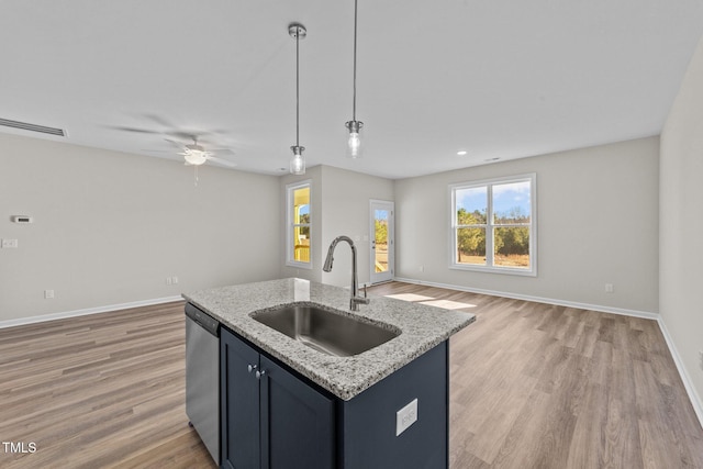 kitchen featuring pendant lighting, dishwasher, an island with sink, sink, and light stone counters