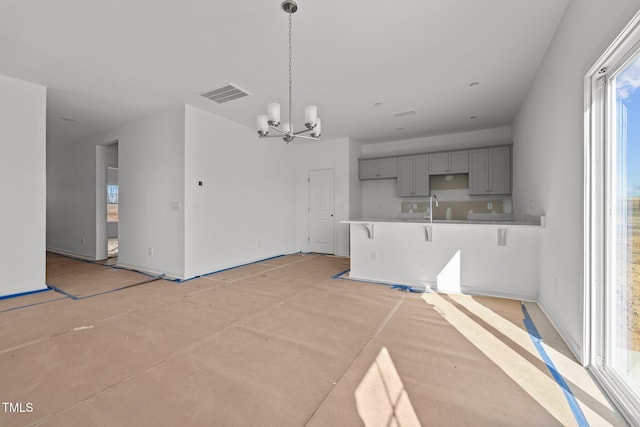 kitchen featuring a kitchen bar, sink, gray cabinetry, decorative light fixtures, and a notable chandelier