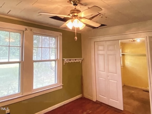 unfurnished bedroom featuring crown molding, dark wood-type flooring, ceiling fan, and a closet