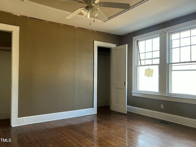 unfurnished bedroom featuring multiple windows, dark hardwood / wood-style flooring, ceiling fan, and a closet