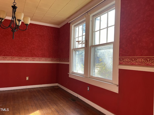 empty room featuring wood-type flooring, a chandelier, and crown molding