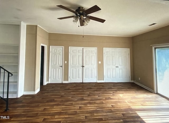 unfurnished bedroom featuring two closets, dark wood-type flooring, and ceiling fan