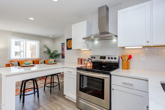 kitchen featuring white cabinetry, wall chimney exhaust hood, stainless steel electric stove, and light hardwood / wood-style floors