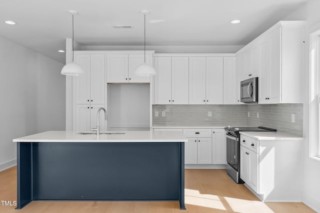 kitchen featuring decorative light fixtures, stainless steel appliances, white cabinets, and a center island with sink