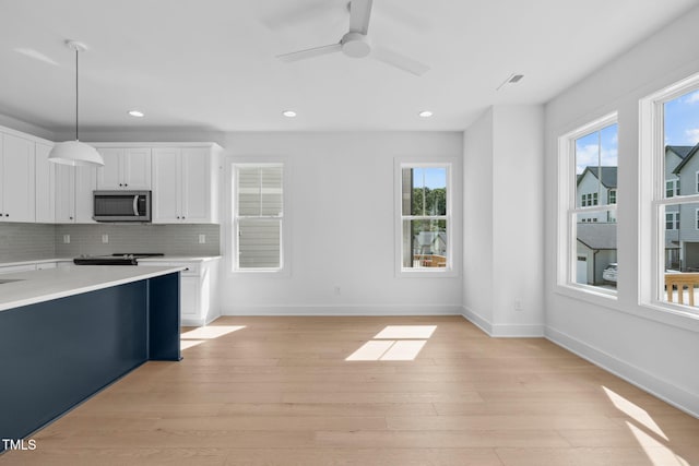 kitchen with decorative light fixtures, white cabinets, decorative backsplash, ceiling fan, and light hardwood / wood-style flooring