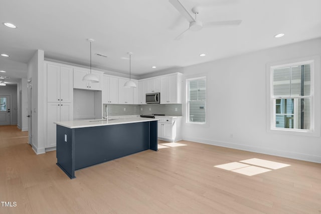 kitchen with white cabinetry, tasteful backsplash, hanging light fixtures, light wood-type flooring, and a kitchen island with sink