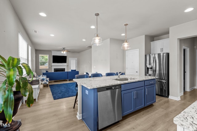 kitchen with blue cabinetry, appliances with stainless steel finishes, a kitchen island with sink, white cabinets, and decorative light fixtures