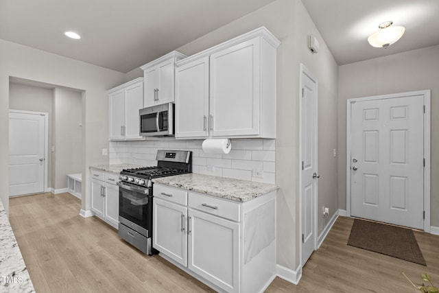 kitchen with appliances with stainless steel finishes, tasteful backsplash, white cabinetry, light hardwood / wood-style floors, and light stone countertops