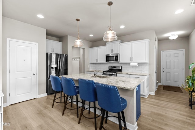 kitchen featuring sink, backsplash, stainless steel appliances, an island with sink, and white cabinets