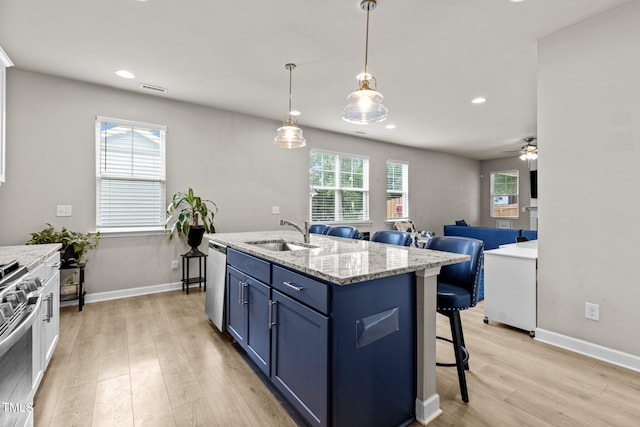 kitchen featuring blue cabinets, sink, appliances with stainless steel finishes, pendant lighting, and a kitchen island with sink