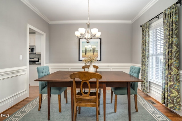 dining room with hardwood / wood-style flooring, crown molding, and an inviting chandelier