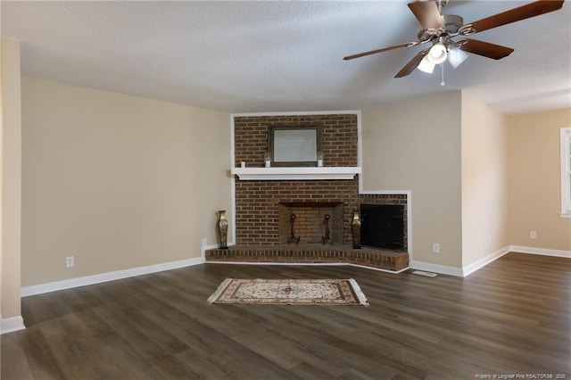 unfurnished living room with ceiling fan, dark hardwood / wood-style flooring, a brick fireplace, and a textured ceiling