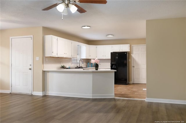 kitchen featuring sink, black fridge, white cabinetry, dark hardwood / wood-style floors, and kitchen peninsula