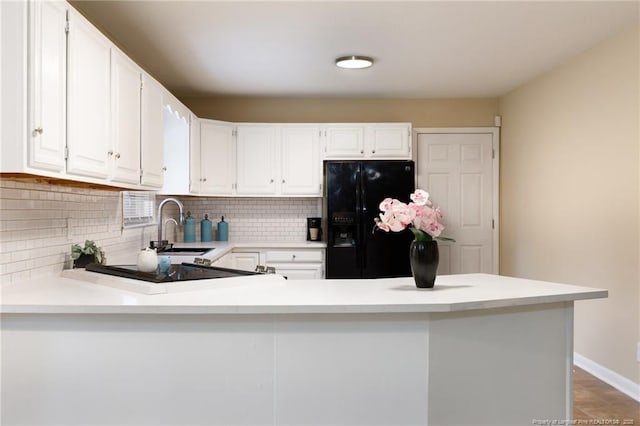 kitchen with white cabinetry, sink, kitchen peninsula, and black fridge