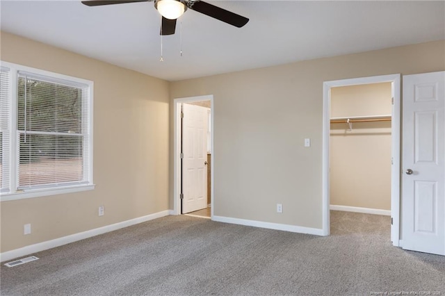 unfurnished bedroom featuring light carpet, a walk in closet, a closet, and ceiling fan