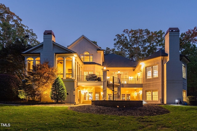 back house at dusk featuring a lawn, french doors, and a balcony