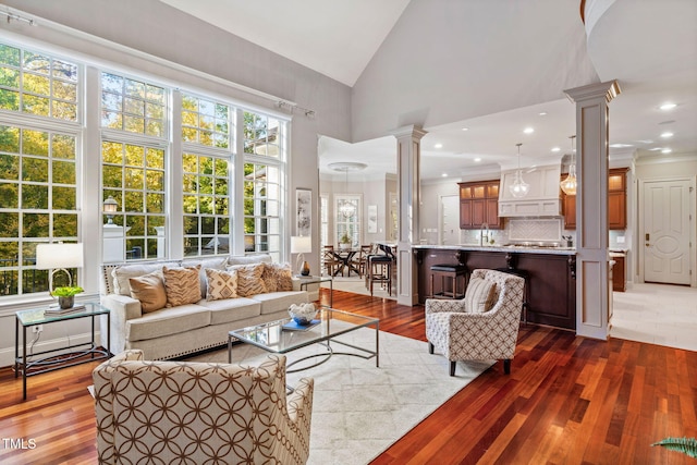 living room with crown molding, high vaulted ceiling, hardwood / wood-style floors, and ornate columns